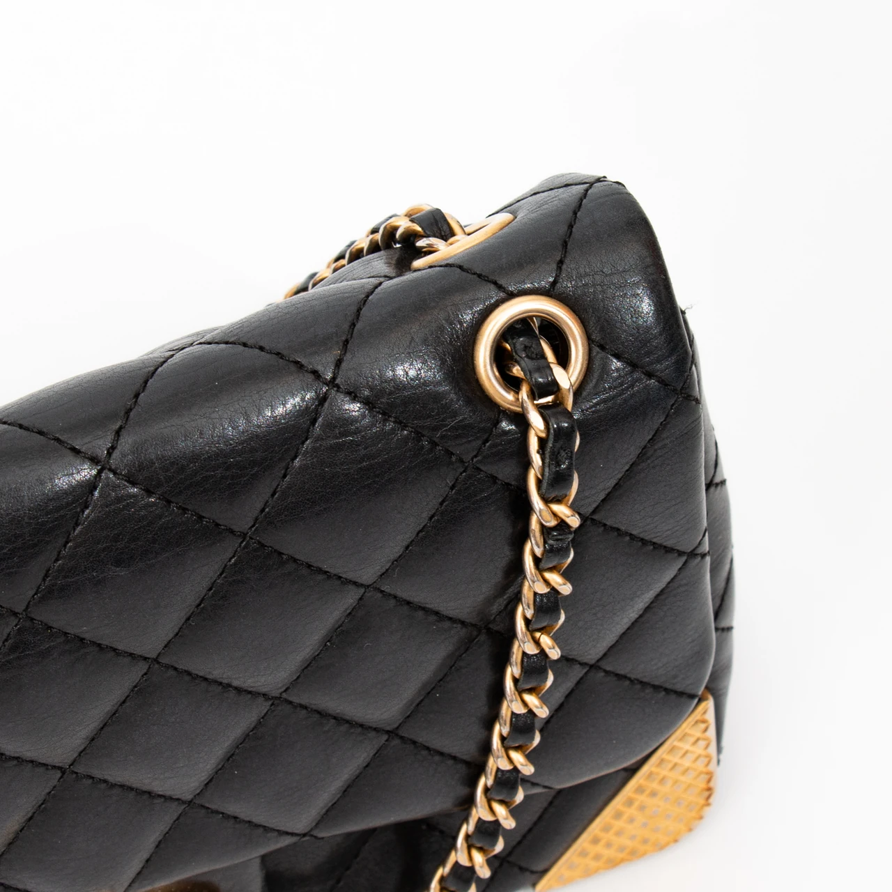 Supplied detail photograph: black quilted leather, stitching, a gold leather-woven chain and metal eyelet